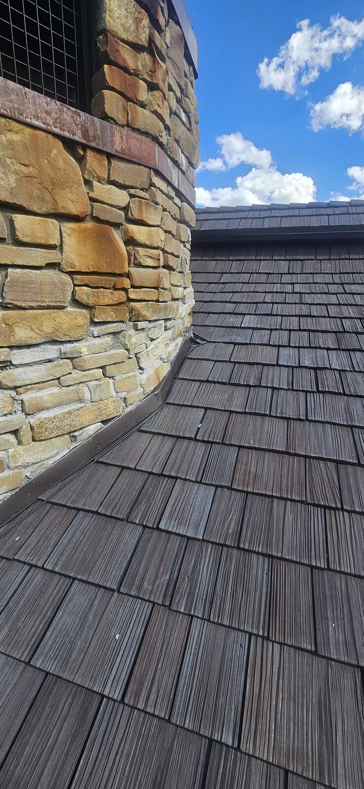 Cedar shake roof with soldered copper valley against a stone chimney