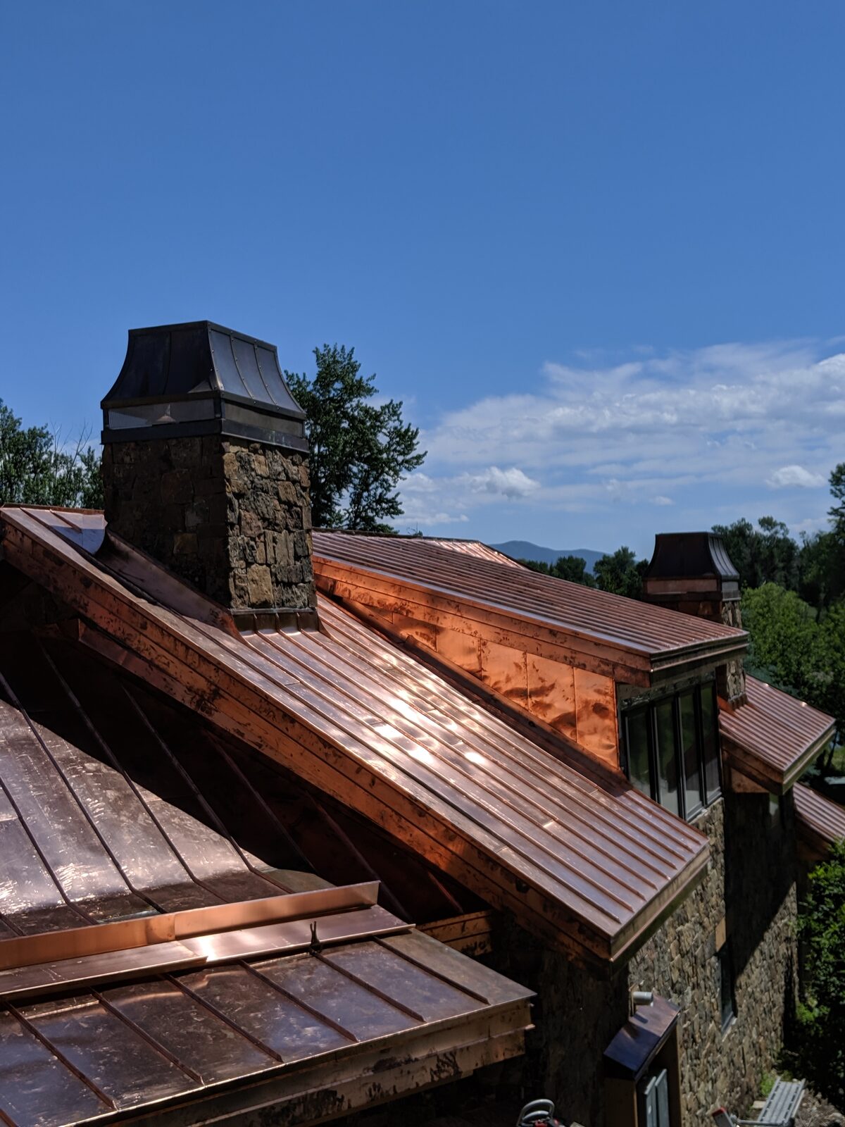 Copper standing-seam roof with stone chimney and mountain backdrop